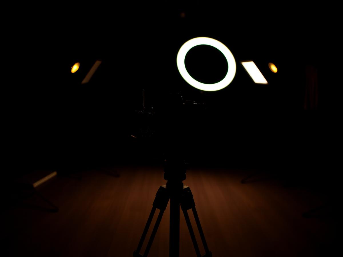 Camera on a tripod facing a ring light in a dark content studio